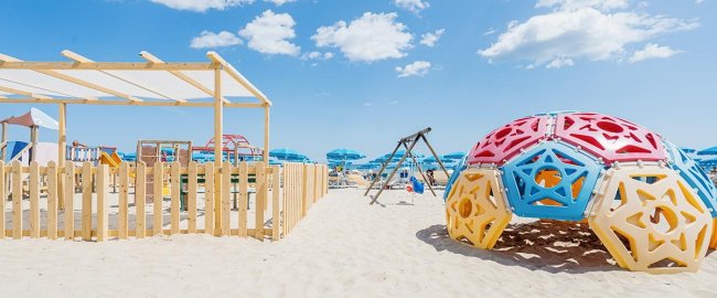 Spiaggia con giochi colorati e ombrelloni blu.
