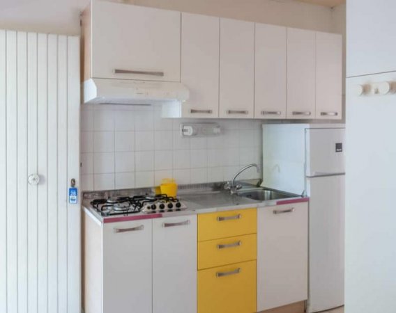 Cucina compatta con mobili bianchi e gialli.