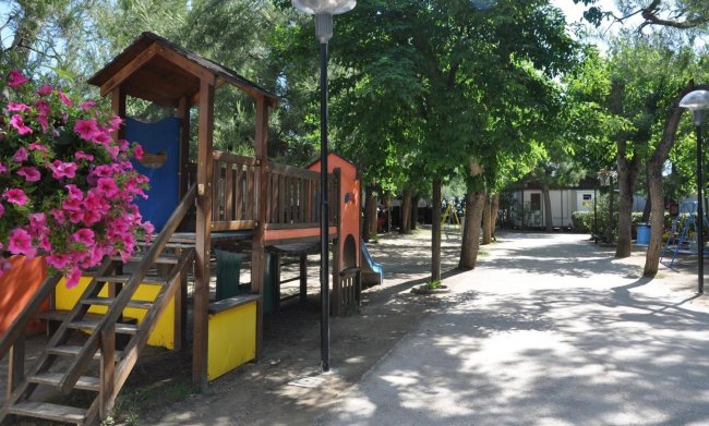 Parco giochi con scivoli e panchine ombreggiate.