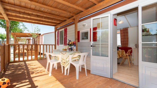 Veranda in legno, tavolo con sedie bianche, porta aperta.