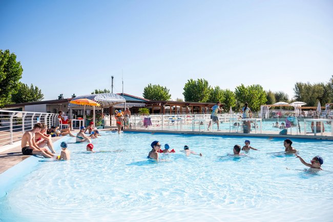 Persone in piscina con sole e ombrelloni.