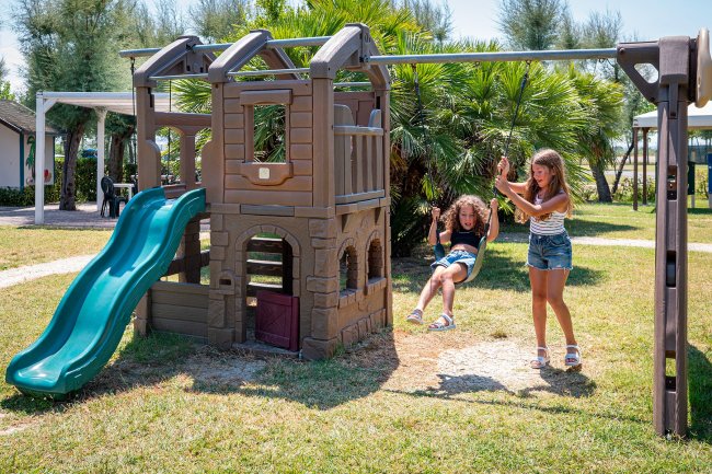 Bambine giocano su altalena e scivolo.