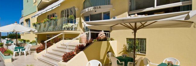 Terrazza di un hotel con ombrelloni e sedie bianche.