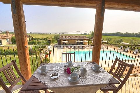 Tavolo apparecchiato su balcone con vista su piscina e campo aperto.