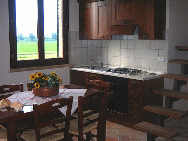Cucina rustica con tavolo in legno, cestino di fiori e finestra aperta su un panorama verde.
