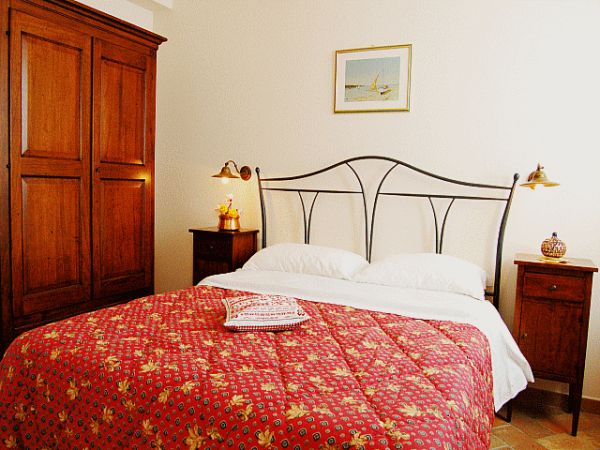 Camera con letto matrimoniale, copriletto rosso, comodini e armadio in legno.