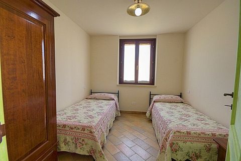 Stanza con due letti singoli e copriletti floreali, dotata di finestra centrale.