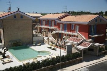 Edificio residenziale moderno con piscina e lettini in un cortile soleggiato.
