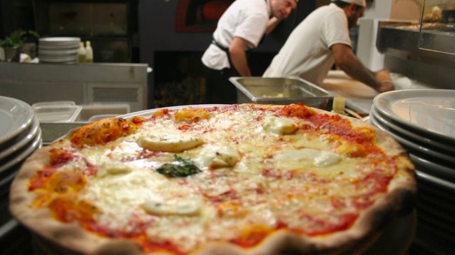Pizza margherita con cuochi sullo sfondo.