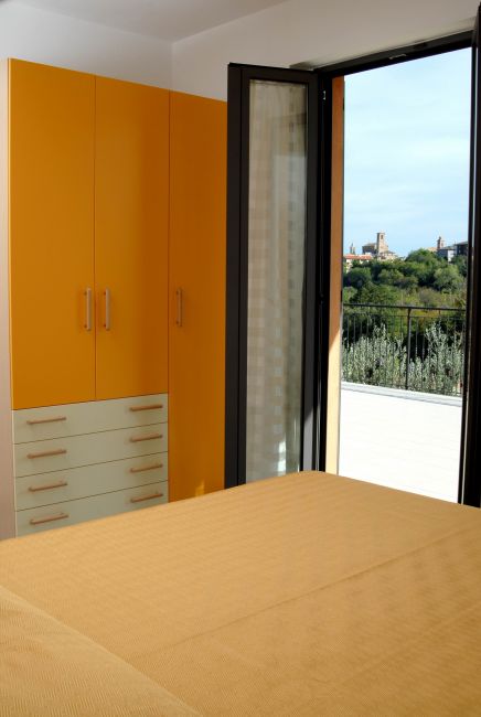 Camera da letto con armadio arancione e porta aperta su un terrazzo con vista panoramica.