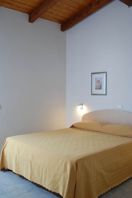 Camera da letto con letto matrimoniale e copriletto giallo, soffitto in legno.