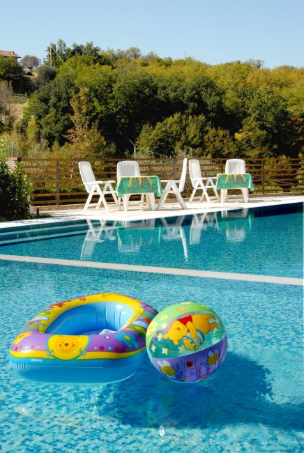 Piscina con giocattoli gonfiabili colorati e sedie bianche in legno.