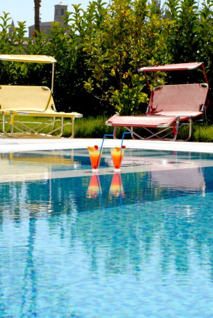 Piscina con due cocktail colorati e sedie a sdraio rosse e gialle.
