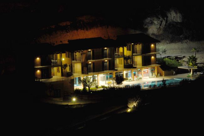 Edificio moderno illuminato di notte, con balconi e piscina, incorniciato da colline.