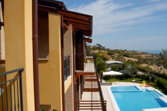 Vista laterale di un edificio con piscina, ombrellone e colline sullo sfondo.